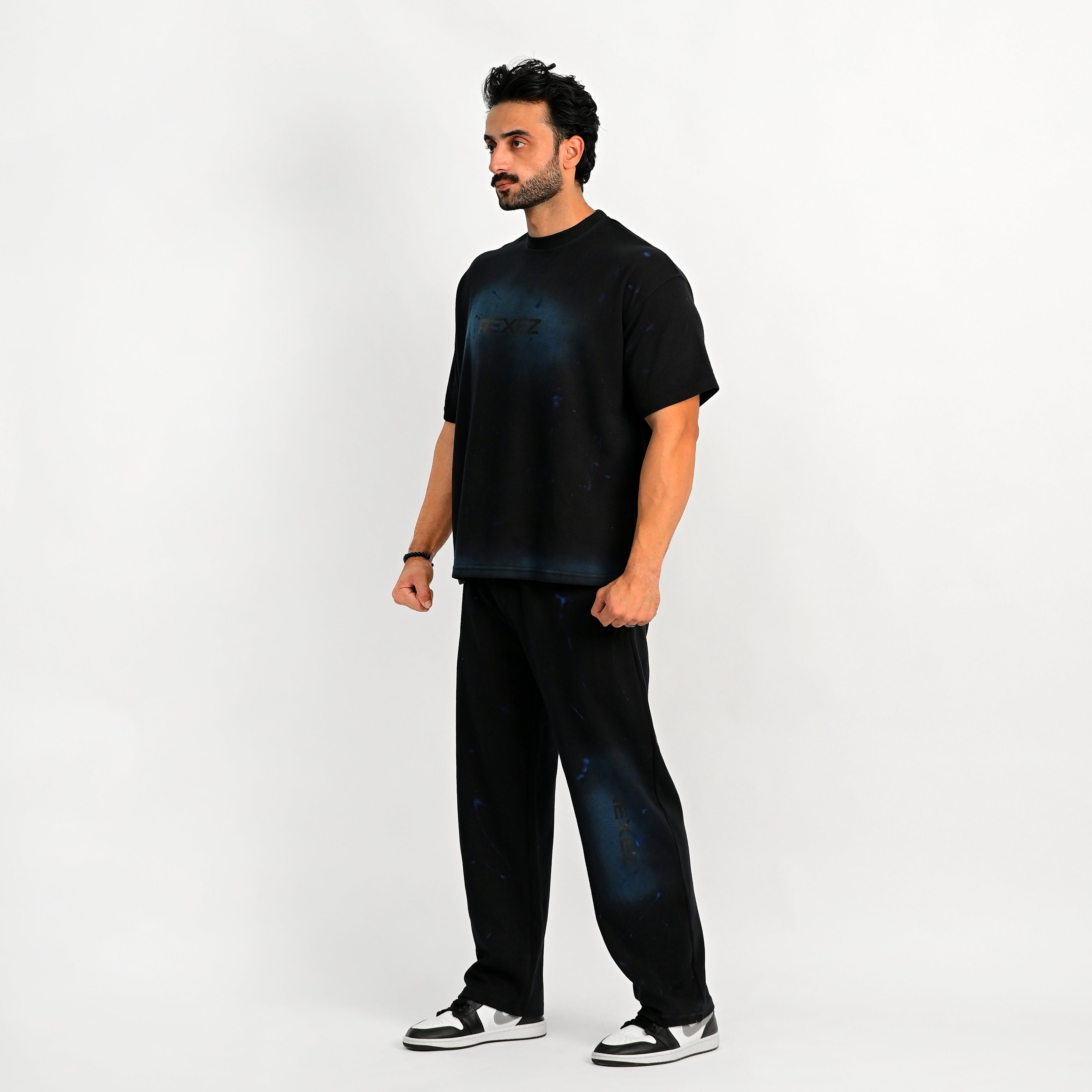 Man wearing a black outfit with blue splatter design on a white background