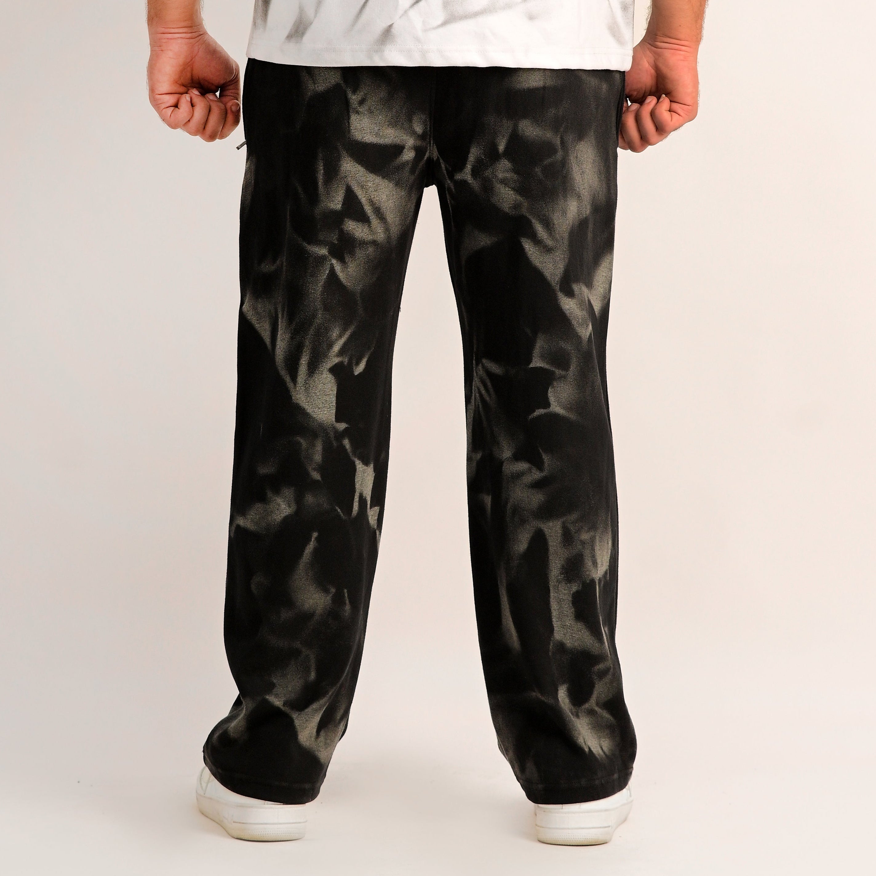 Person wearing a white shirt with abstract design and black patterned pants on a plain background