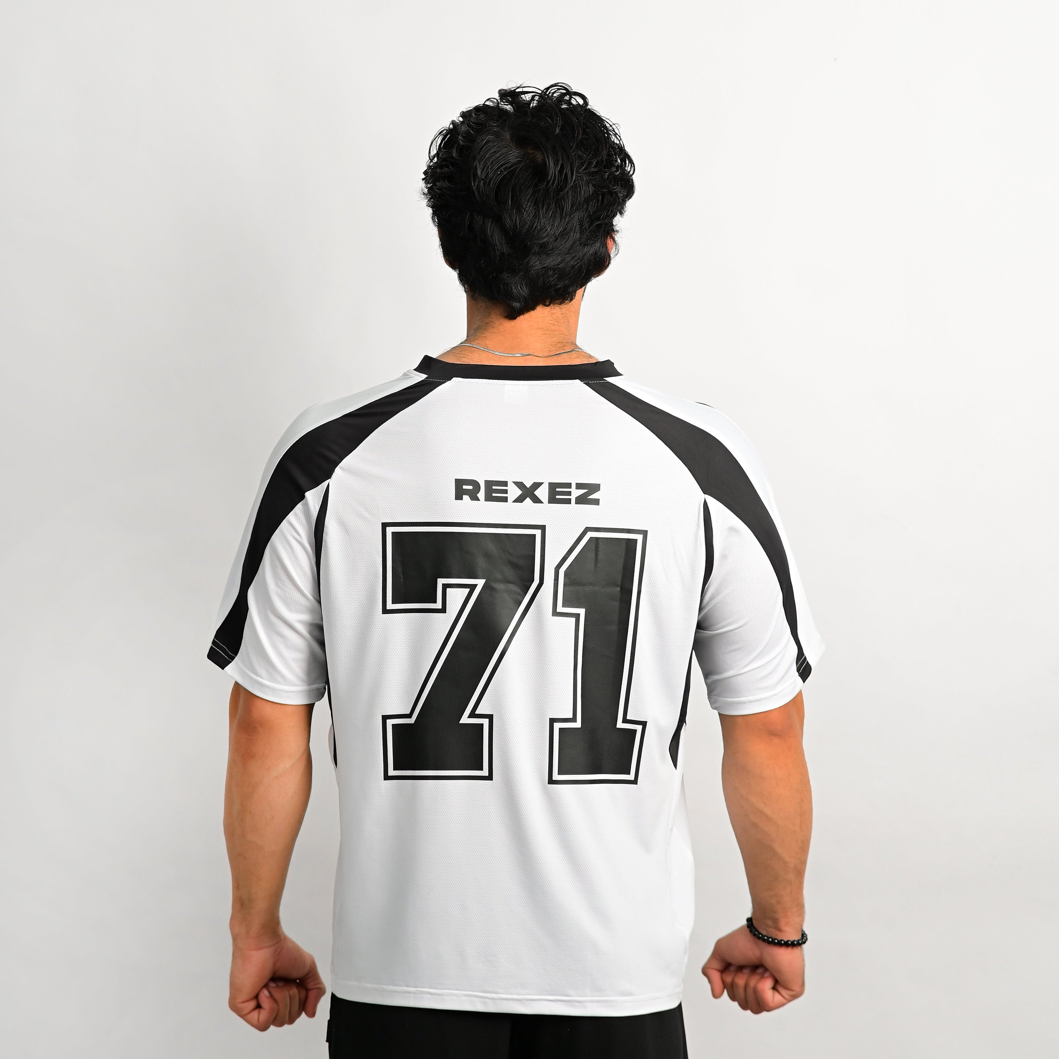 A man shown in profile wearing a white athletic jersey with bold black side panels and a small circular crest on the chest, photographed against a plain light gray studio background.