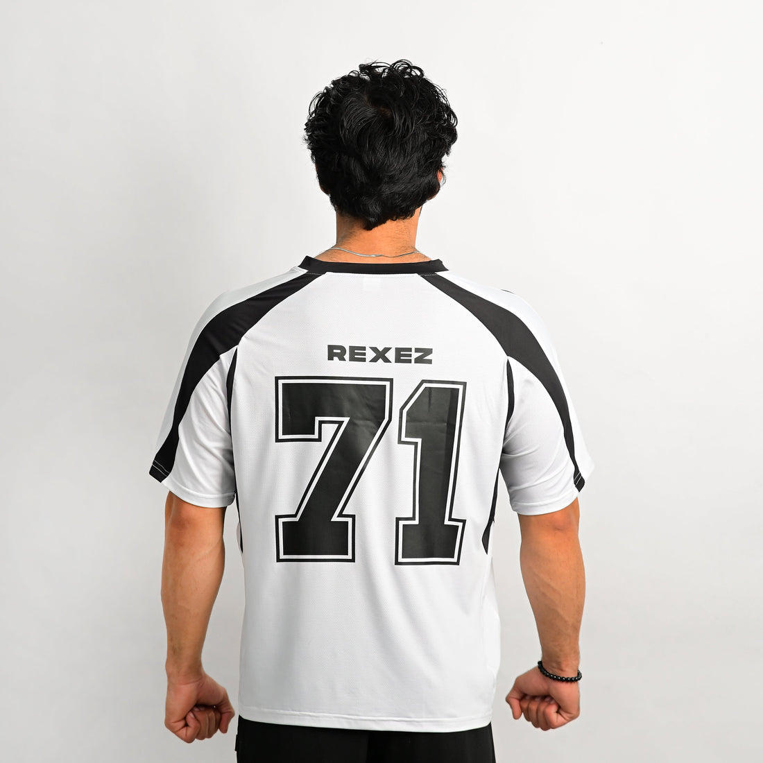 A man shown in profile wearing a white athletic jersey with bold black side panels and a small circular crest on the chest, photographed against a plain light gray studio background.