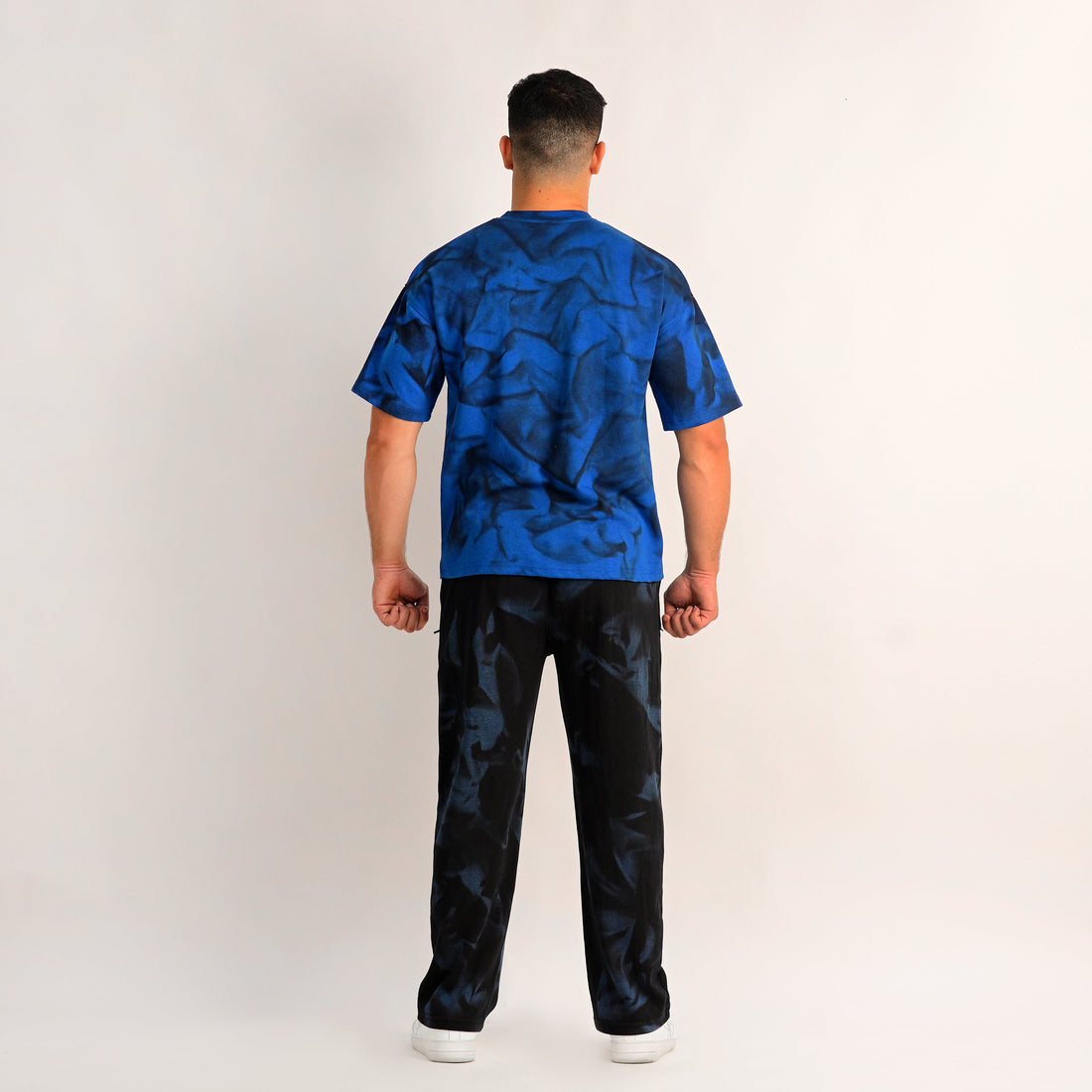 Person wearing a blue patterned shirt and black pants on a white background