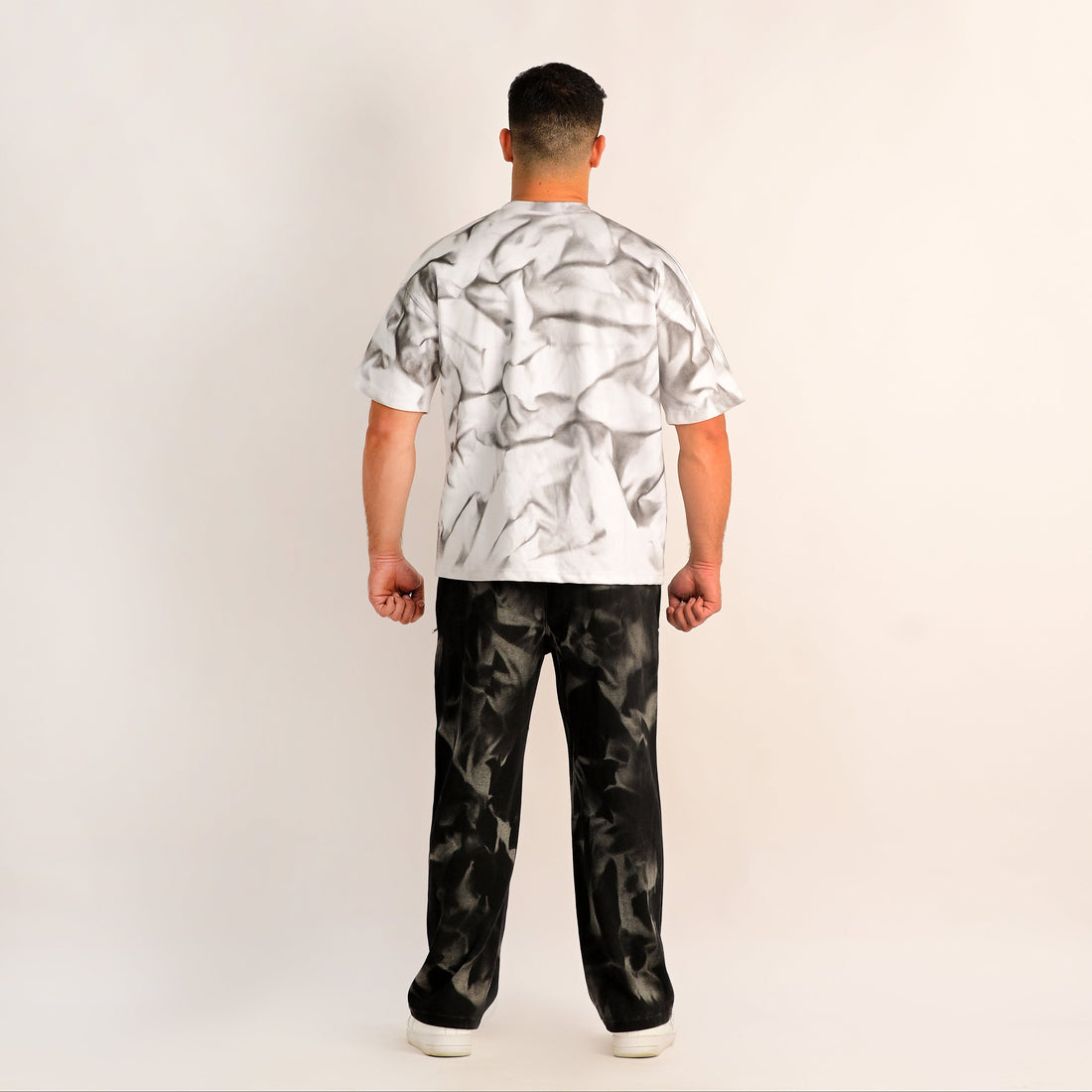 Person wearing a white patterned shirt and black pants on a plain background