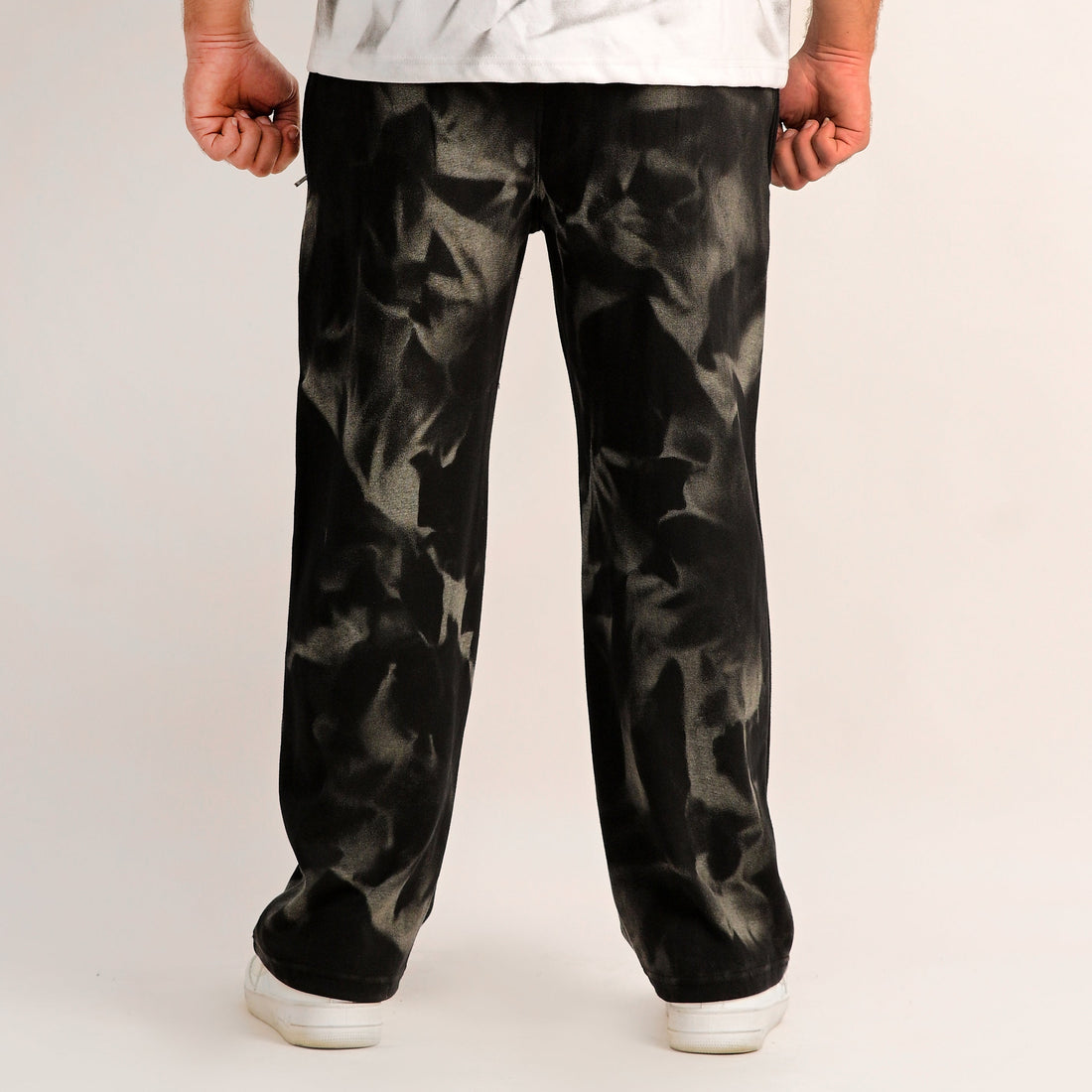 Person wearing a white shirt with abstract design and black patterned pants on a plain background